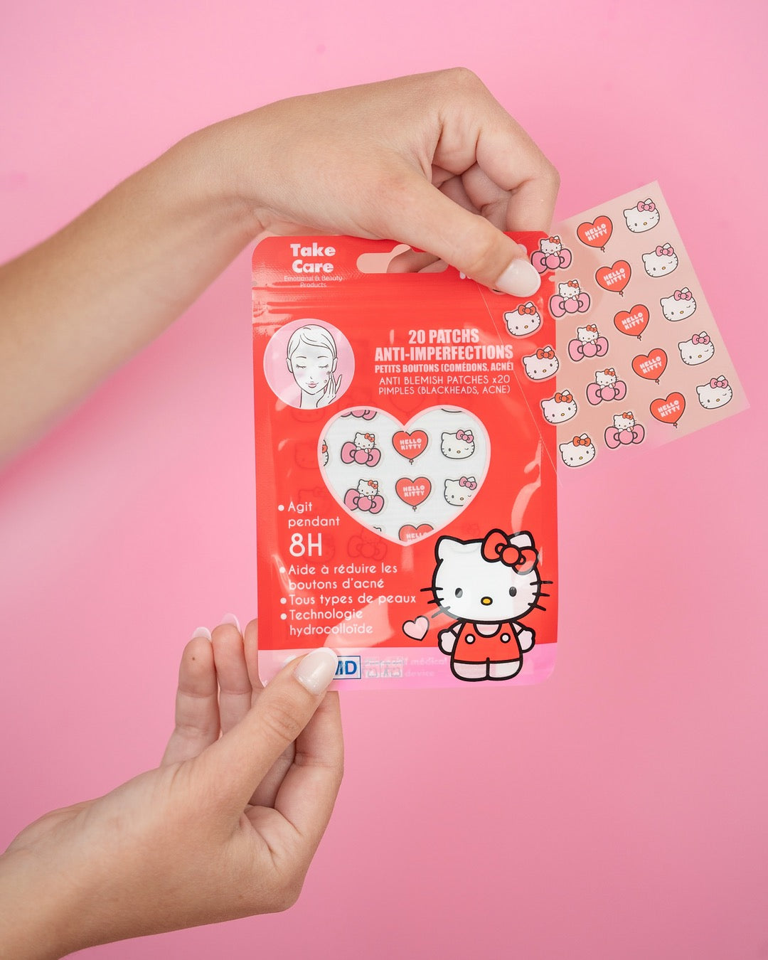 Mains d’une femme sortant la plaquette d’autocollants hydrocolloïdes de son sachet d’emballage rouge sur un fond rose uni.