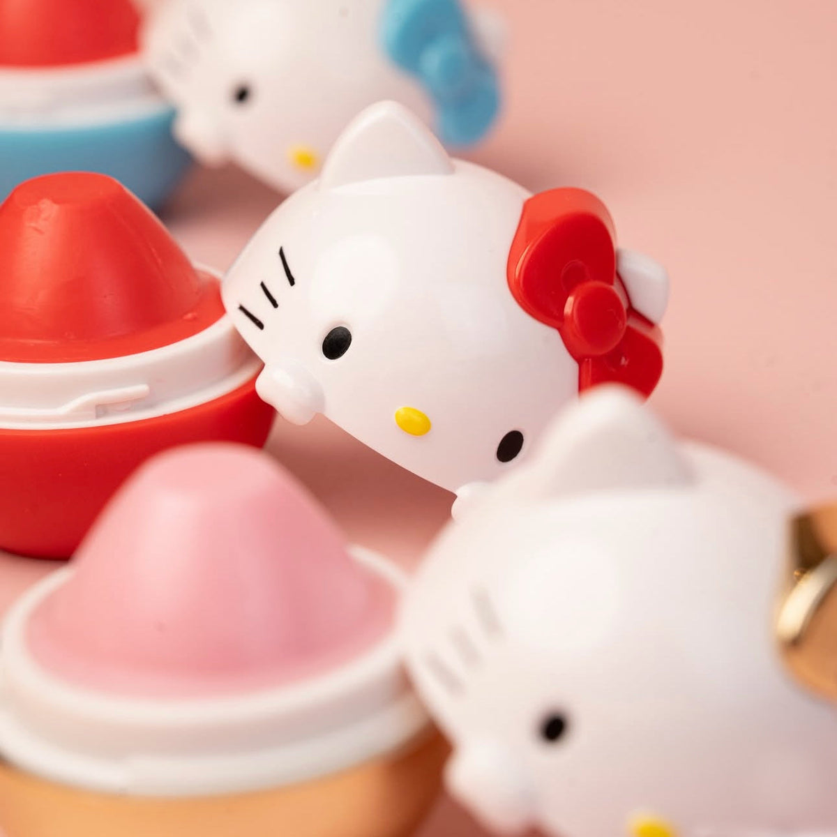 Baumes à lèvres hydratants Hello Kitty en forme de figurines de collection Sanrio sur un fond rose pastel.