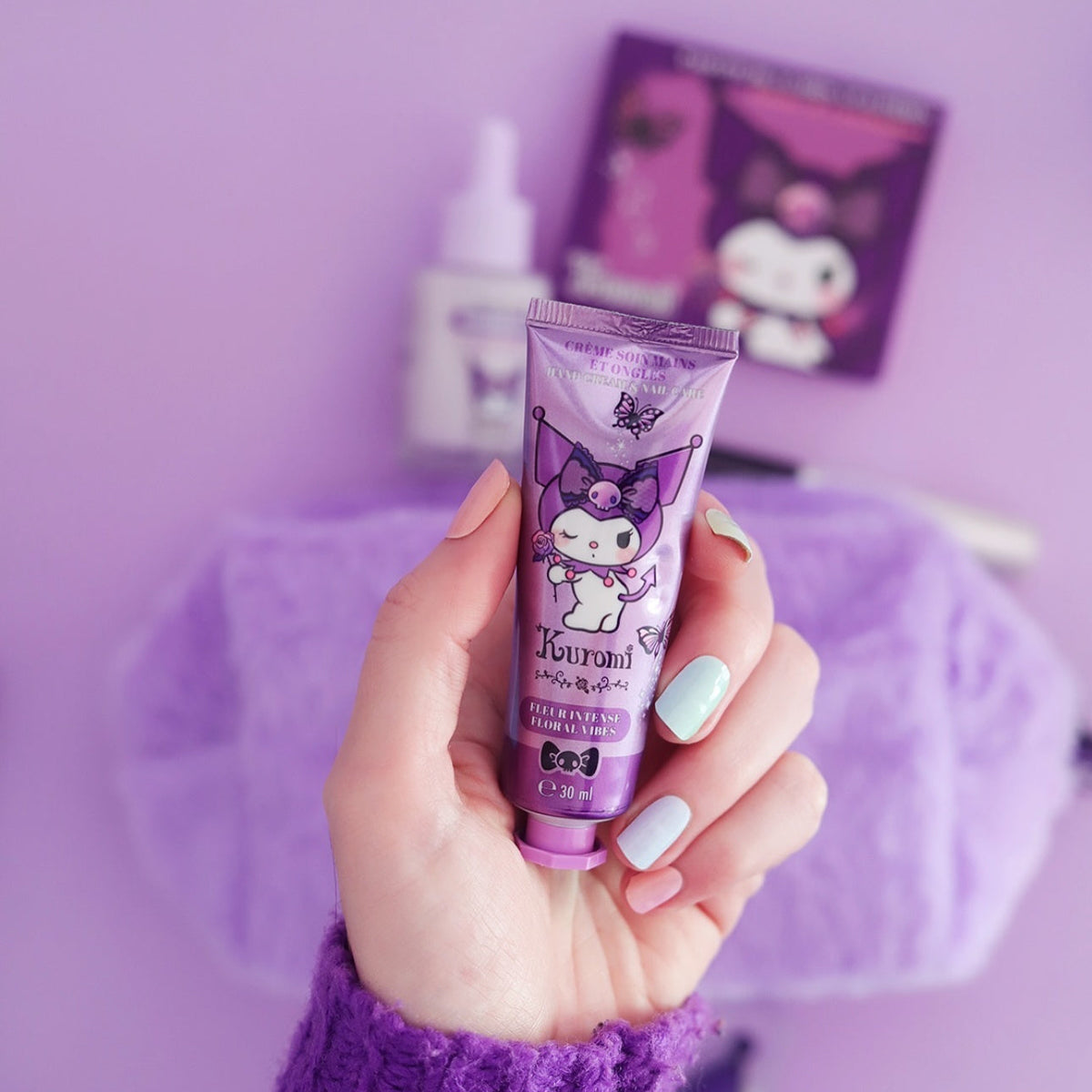Tube de crème soin mains et ongles Kuromi de Sanrio, parfum Fleur Intense, tenu dans une main aux ongles manucurés sur fond violet.