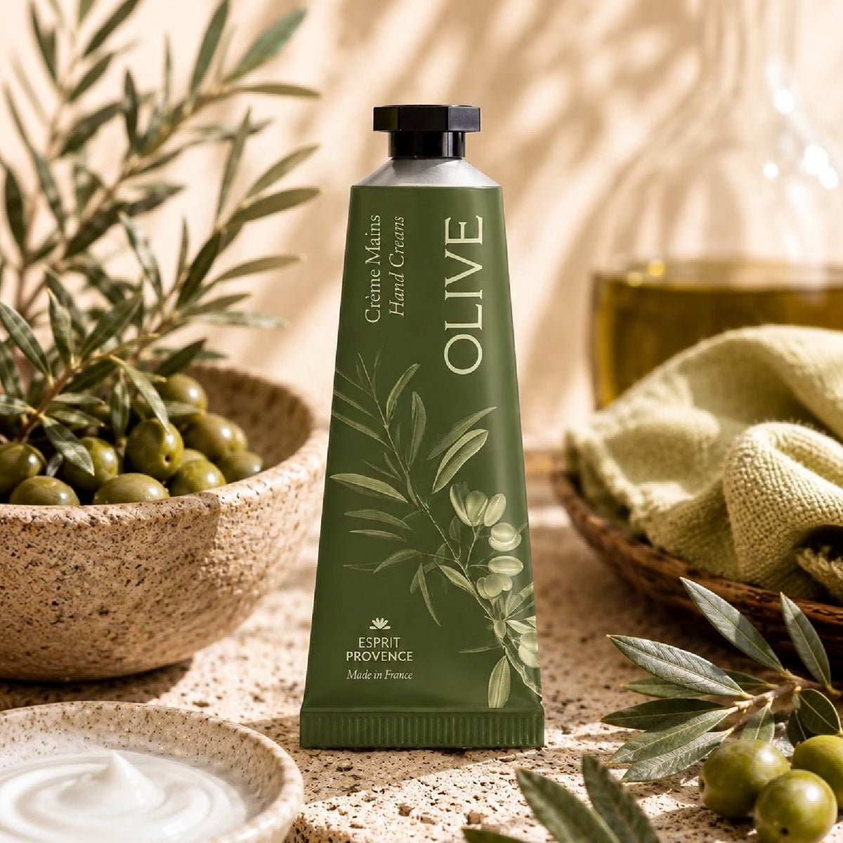 Tube de crème pour les mains Plantes & Parfums Provence au lait d'ânesse bio, posé debout sur une planche en bois à côté d'un lys blanc et de flocons d'avoine.