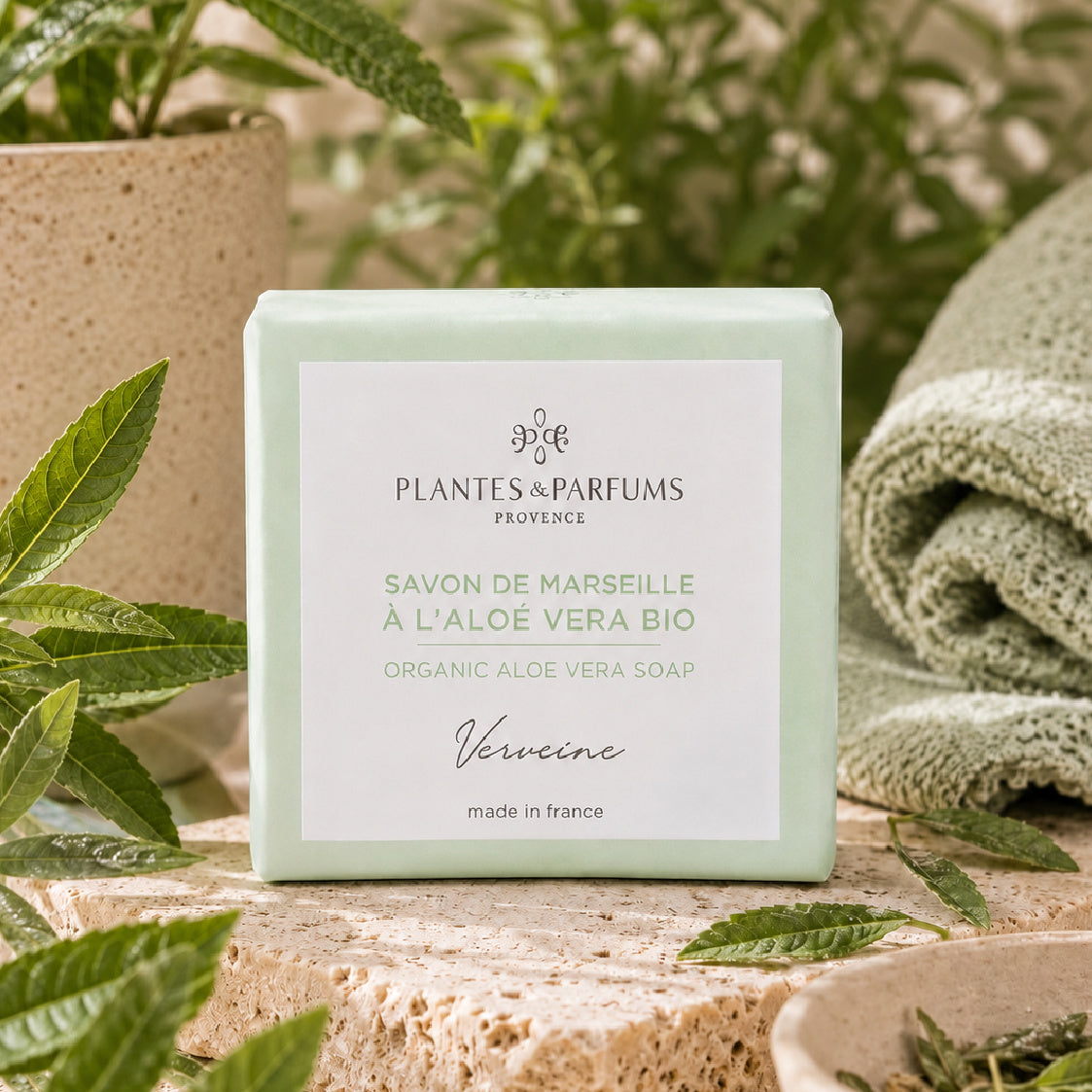 Portrait de profil d'une femme souriante regardant vers le haut, tenant délicatement un pain de savon artisanal vert clair entre ses mains, avec un papillon illustré dans le coin supérieur droit.