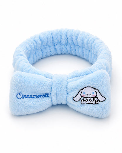 Bandeau de tête élastique en peluche bleu ciel avec un grand nœud central brodé du nom et du personnage Cinnamoroll de Sanrio.