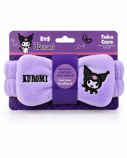 Vue de face d'un bandeau à cheveux élastique en peluche violette avec un grand nœud brodé Kuromi Sanrio présenté dans son emballage  cartonné mauve.