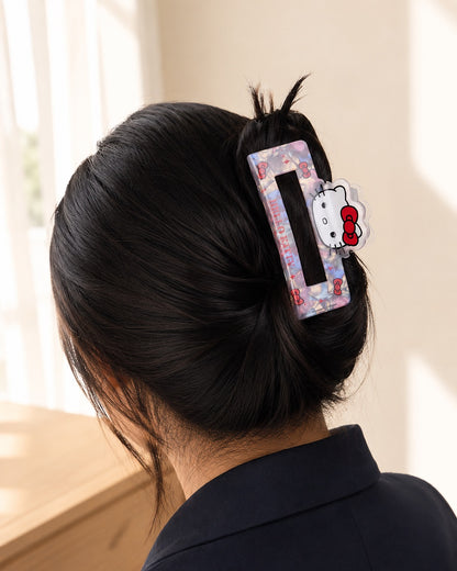 Vue arrière des cheveux bruns d’une femme relevés à l’aide de la grande pince à cheveux rose nacrée Hello Kitty avec vue de fond d'une fenêtre.