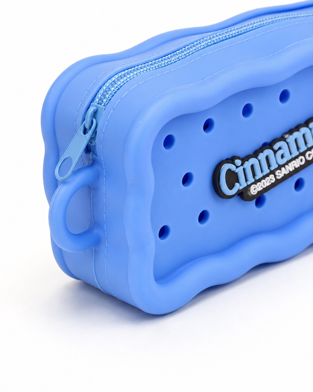 Trousse rectangulaire en silicone bleu avec des perforations contenant trois pins amovibles du personnage Cinnamoroll et de desserts.
