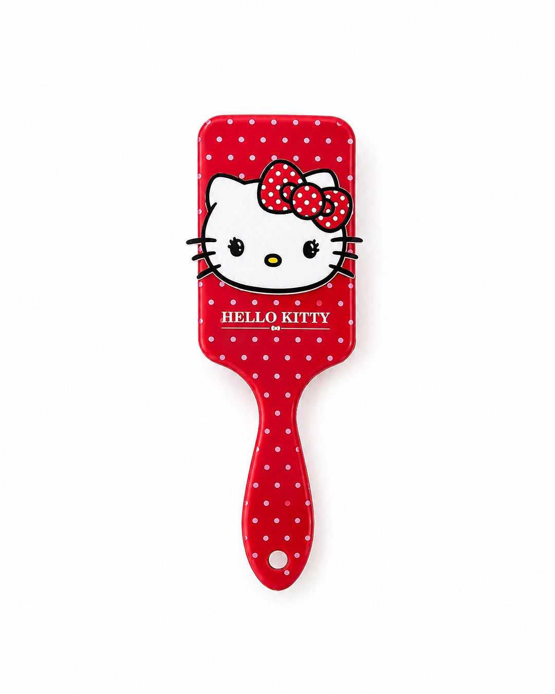 Vue de face d’une brosse à cheveux rectangulaire rouge à pois blancs, ornée d’une grande figurine Hello Kitty en relief avec son nœud rouge.