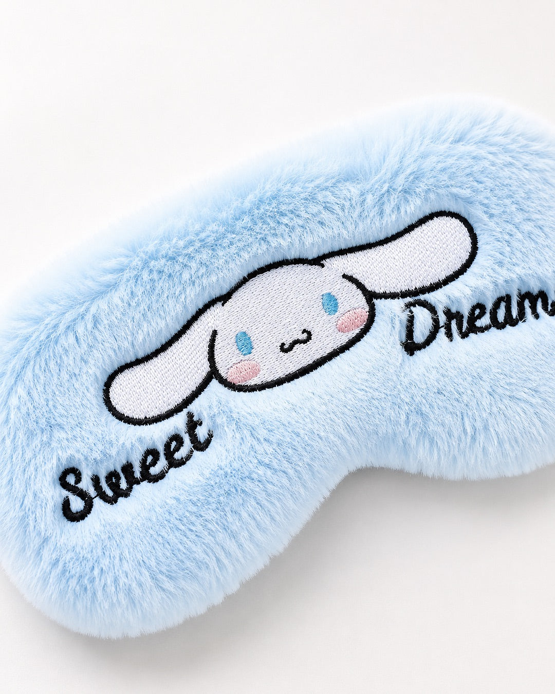 Masque de nuit en peluche bleu doux avec broderie de Cinnamoroll et texte Sweet Dreams sur son emballage d'origine.