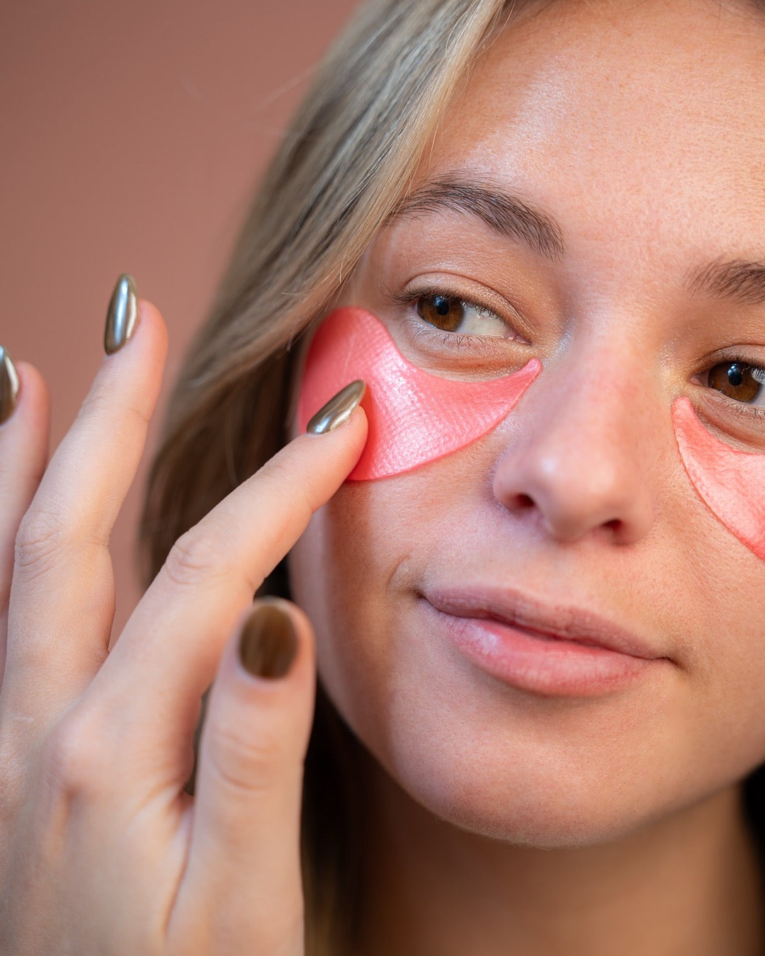 Gros plan sur le visage d'une femme portant un patch hydrogel rose sous l'œil pour hydrater le contour du regard.