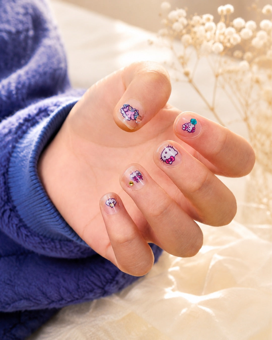 Gros plan sur une manucure terminée montrant des ongles naturels décorés avec les autocollants Hello Kitty et des strass étincelants.