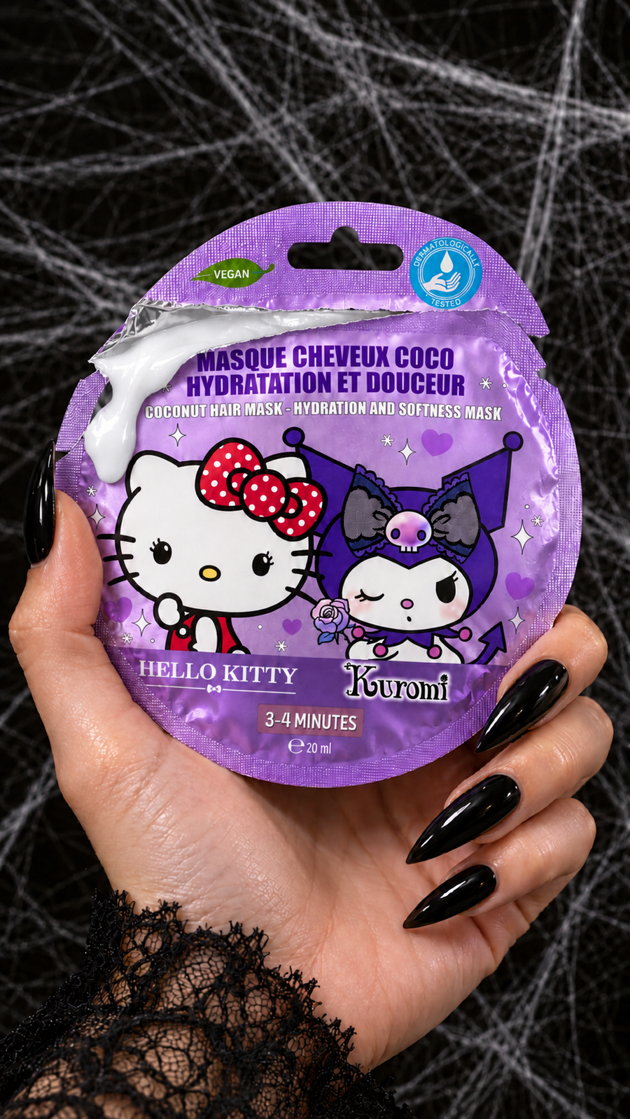 Masque capillaire Hello Kitty et Kuromi à la noix de coco, sachet mauve tenu dans une main aux ongles noirs sur fond de toiles d'araignée d'Halloween