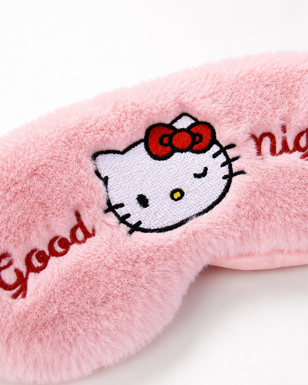 Gros plan détaillé sur la broderie centrale du masque de nuit, montrant le visage d’Hello Kitty faisant un clin d’œil et le texte texturé.