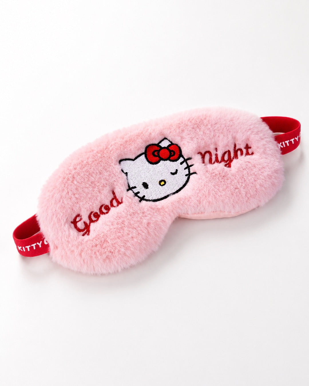 Vue de face d’un masque de nuit en peluche rose Hello Kitty avec l’inscription brodée Good Night et une bande élastique rouge.