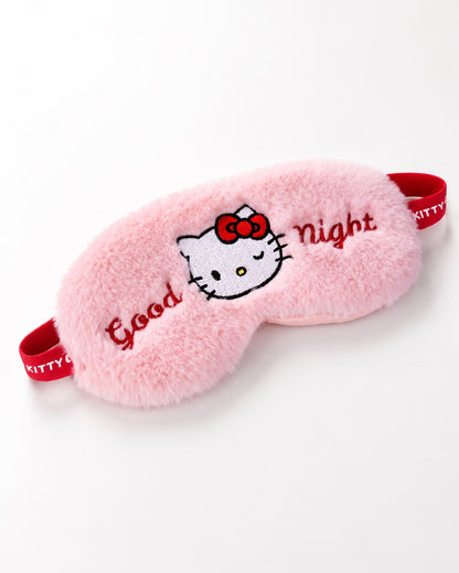 Vue de face d’un masque de nuit en peluche rose Hello Kitty avec l’inscription brodée Good Night et une bande élastique rouge.