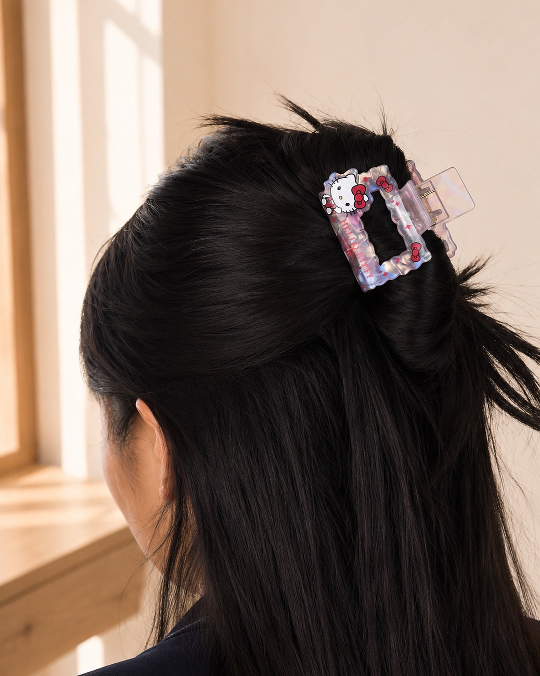Vue de trois quarts d’un chignon flou sur cheveux bruns attaché par la petite pince rectangulaire Hello Kitty près d’une fenêtre.