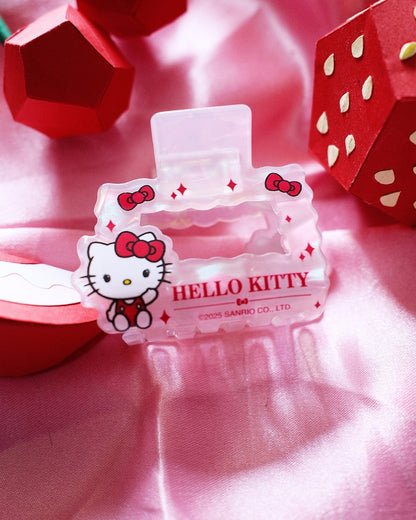 Petite pince à cheveux nacrée Hello Kitty posée à plat sur un tissu satiné rose à côté de fraises décoratives en papier.
