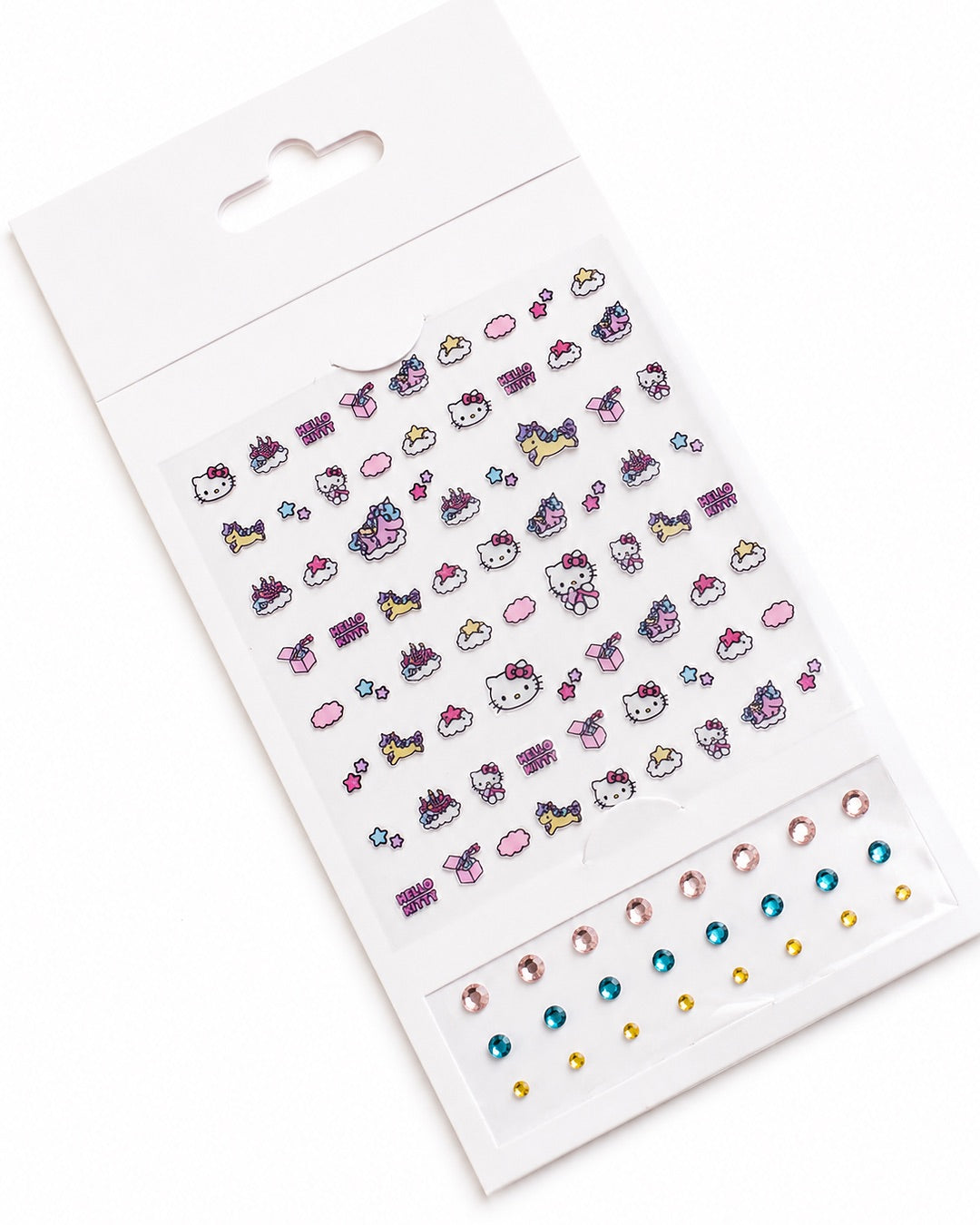 Plaquette d’autocollants pour ongles Hello Kitty sortie de son emballage, accompagnée de trois rangées de strass colorés facettés.