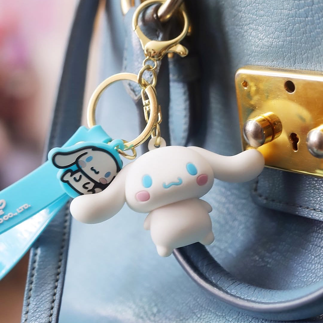 Porte-clé 3D Cinnamoroll officiel de Sanrio avec attache dorée, accroché à un sac à main bleu en cuir.