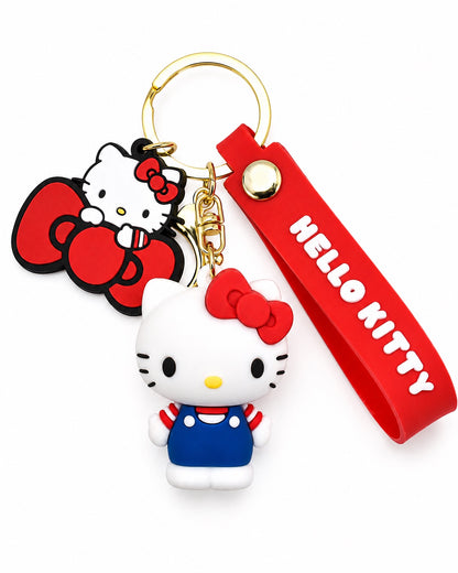 Vue de face d’un porte-clés premium Hello Kitty avec une figurine 3D en salopette bleue, un grand charm en caoutchouc et une dragonne rouge.
