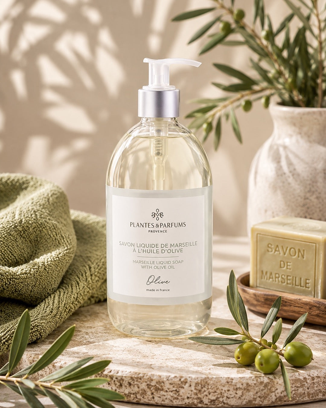 Une bouteille pompe de 500 ml de savon de Marseille liquide, fragrance Olive, Plantes & Parfums, dans son ambiance olfactive.