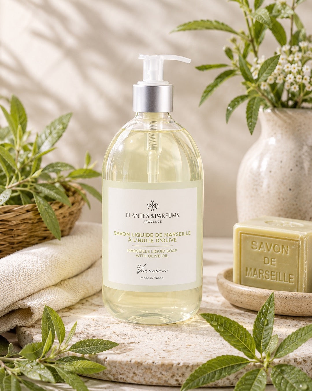 Une bouteille pompe de 500 ml de savon de Marseille liquide, fragrance Verveine, Plantes & Parfums, dans son ambiance olfactive.